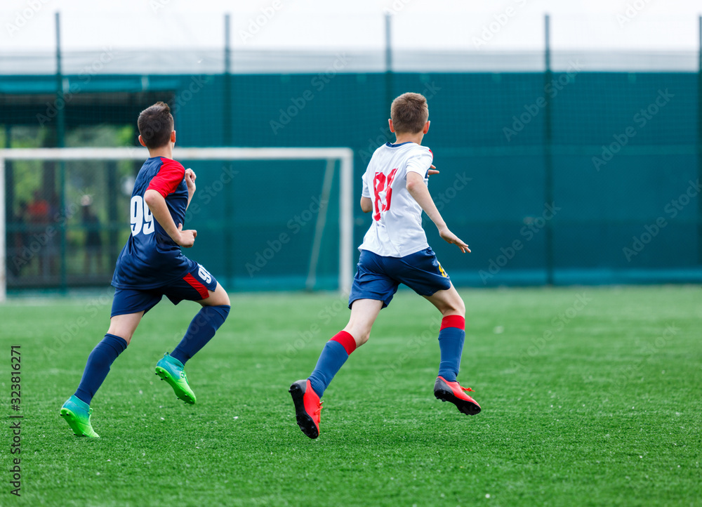 Obraz premium Boys in white and blue sportswear plays football on field, dribbles ball. Young soccer players with ball on green grass. Training, football, active lifestyle for kids concept 