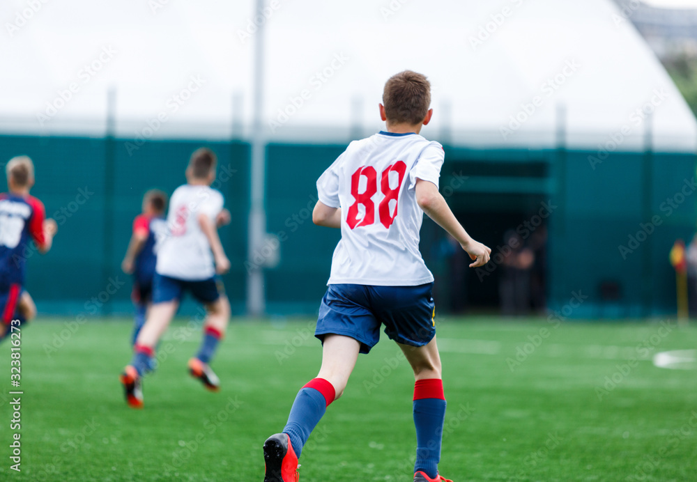 Obraz premium Chłopcy w biało-niebieskich strojach sportowych grają w piłkę nożną na boisku, dryblują piłkę. Młodzi piłkarze z piłką na zielonej trawie. Trening, piłka nożna, aktywny tryb życia dla koncepcji dzieci