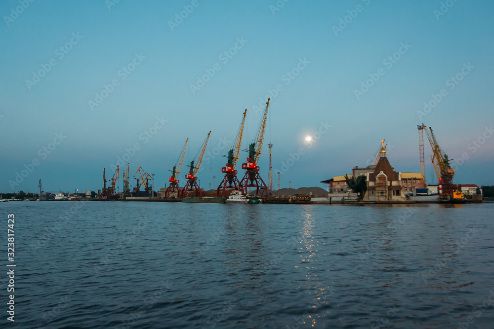 Harbor cargo cranes on eveinng sky background