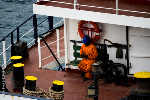 Фотография Seaman seated on bench in a ship with orange coverall using cell phone