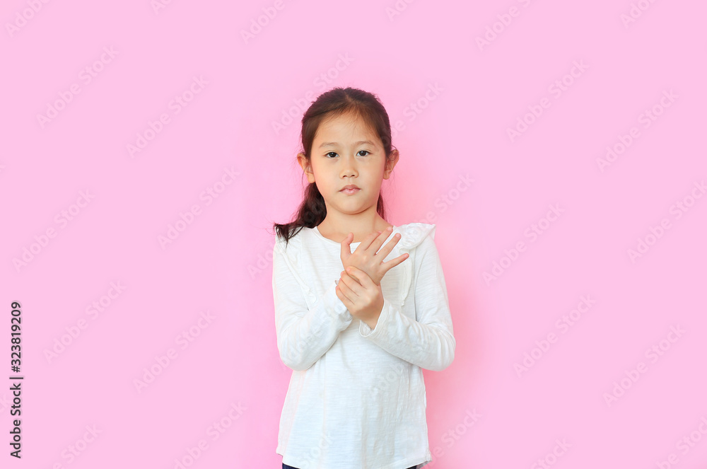 Portrait little asian child girl suffering pain on hands and fingers isolated on pink background. Unhappy kid with expression touching hand with painful gesture. Portrait little asian child girl suffering pain on hands and fingers isolated on pink background. Unhappy kid with expression touching hand with painful gesture.