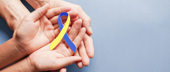Adult and child hands holding blue and yellow ribbon shaped paper, Down syndrome awareness , World down syndrome day