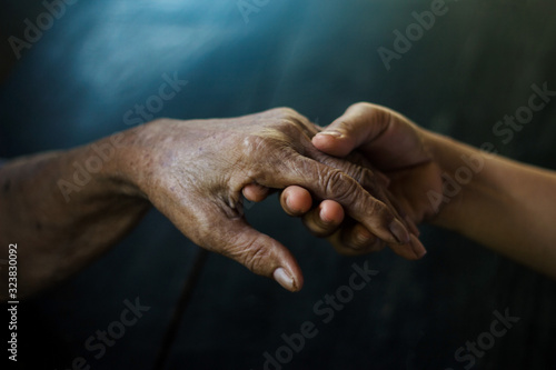 Daughter holding hand of mother elderly that is alzheimer and parkinson patient on dark background.