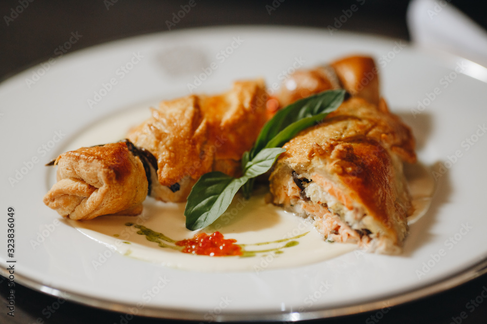 Pie with sauerkraut and fish, Russian kulebyaka. On a white plate and a wooden table, behind a brown tablecloth, side view at an angle, close Pie with sauerkraut and fish, Russian kulebyaka. On a white plate and a wooden table, behind a brown tablecloth, side view at an angle, close