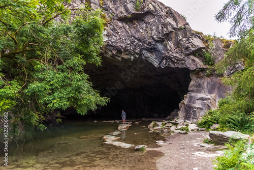 Boy standing on stepping stones in the mouth of a cave in the Lake District National Park in England.