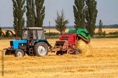 tractor makes big straw roll on yellow field at summer day