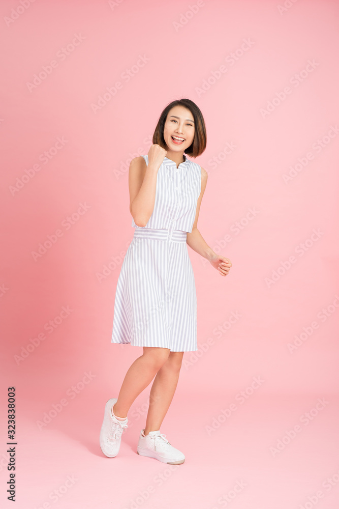 Full length portrait of happy exited pretty girl in elegant light blue dress looking at camera while jumping over pink background Full length portrait of happy exited pretty girl in elegant light blue dress looking at camera while jumping over pink background