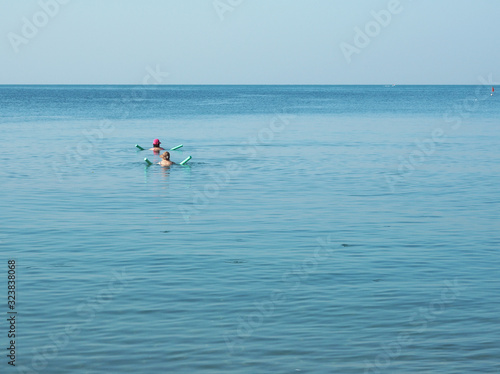 Two Caucasian tourists are swimming in the sea, using floating tubes.  Blue sky and sea water. © Ratchaneeboon