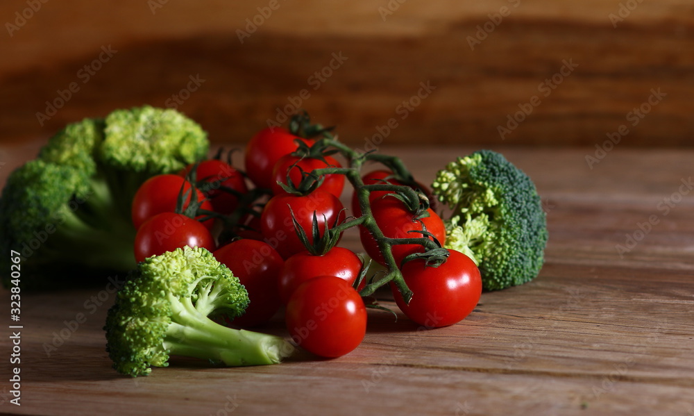 fresh cherry tomatoes on a branch and broccoli on a wooden surface fresh cherry tomatoes on a branch and broccoli on a wooden surface