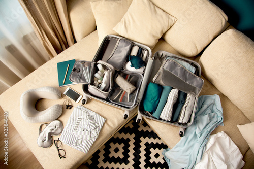 Open grey suitcase with different clothes packed for journey at home. Nordic style minimalism.