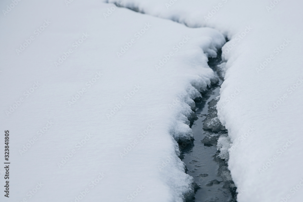 A crack formed on the white snow. Water is visible in the crack.