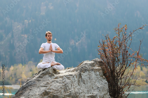 Caucasian yoga man in outdoor meditation sitting on lonely rock island of mountain lake. photo