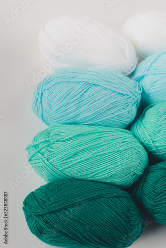 acrylic soft pastel green, azure and white colored wool yarn thread skeins in row on white background, top view, flat lay, vertical stock photo image