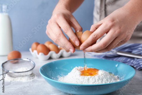 Woman preparing batter for thin pancakes at light grey table, closeup