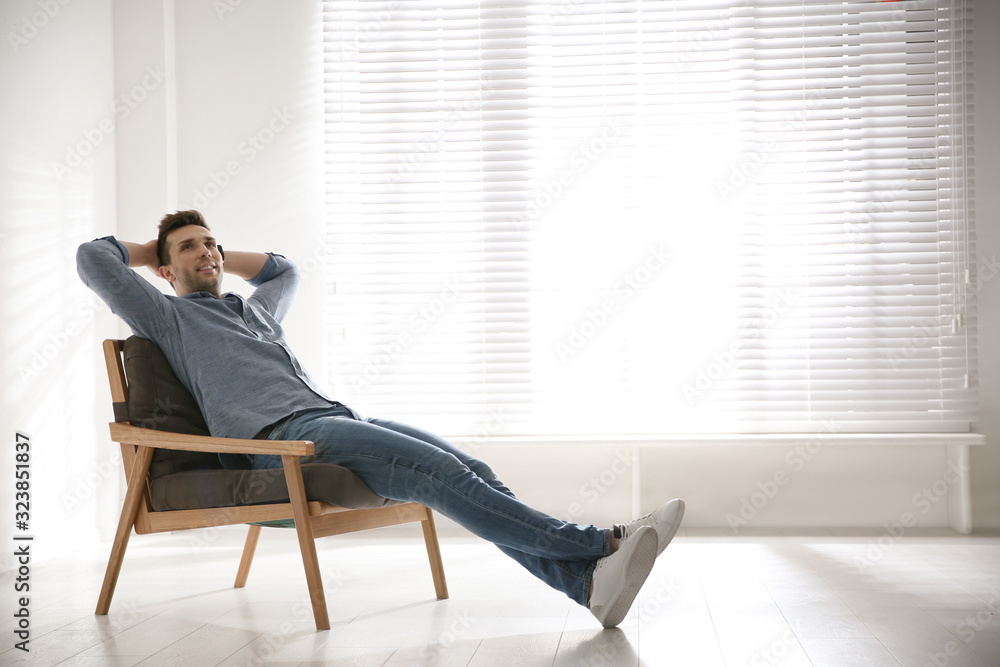 Young man relaxing in armchair near window at home. Space for text