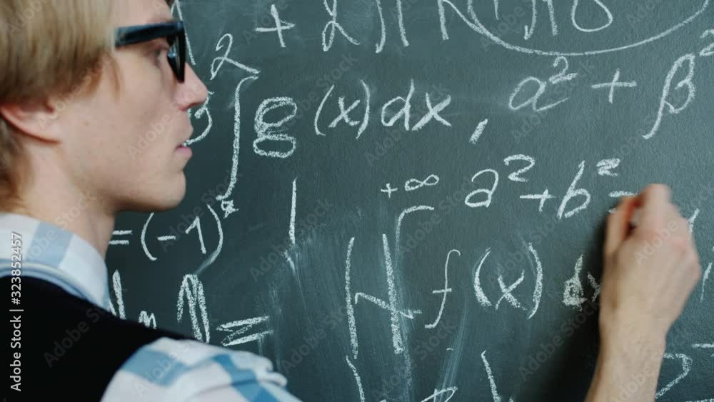 Young mathematician is busy writing formulas on chalkboard working with serious face wearing glasses and casual clothing. People and occupation concept. Young mathematician is busy writing formulas on chalkboard working with serious face wearing glasses and casual clothing. People and occupation concept.