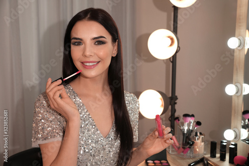 Beautiful young woman applying makeup near mirror in dressing room