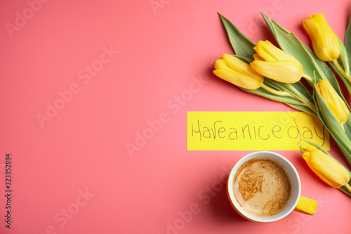 Aromatic morning coffee, beautiful flowers and card with HAVE A NICE DAY wish on pink background, flat lay. Space for text