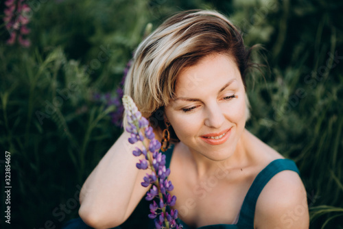 Beautiful romantic woman blonde in a field of purple flowers lupins with a flower. Soft selective focus.