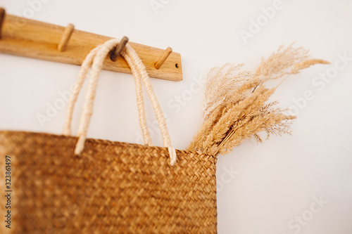 Reusable eco friendly woven straw bag string bag with a bouquet of wheat or ears hanging on a wooden hook on a white wall