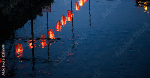 Photograph of the reflection a line of red lanterns and benches at dusk