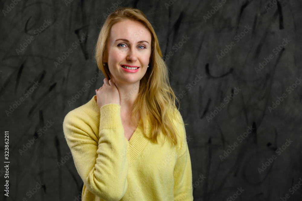 Fototapeta premium Portrait of a stylish business pretty blonde woman in a yellow sweater on a gray background