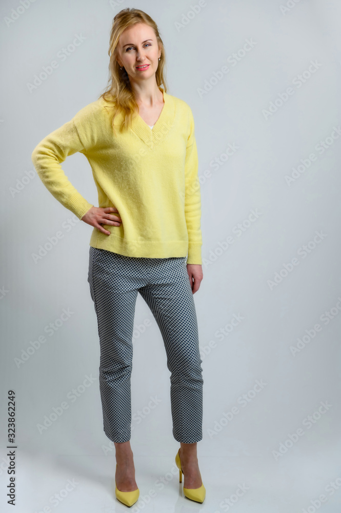 Full-length portrait of a stylish pretty blonde woman in a yellow sweater and gray pants on a white background Full-length portrait of a stylish pretty blonde woman in a yellow sweater and gray pants on a white background