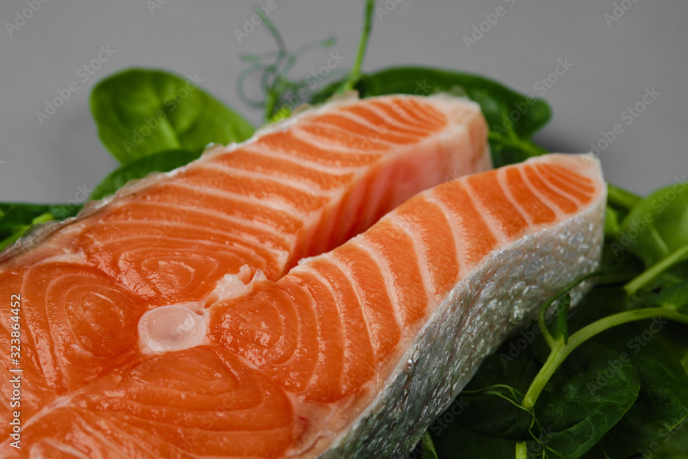 Salmon steak raw fish on spinach leaf and microgreens, prepared for cooking. top view. grey background Salmon steak raw fish on spinach leaf and microgreens, prepared for cooking. top view. grey background