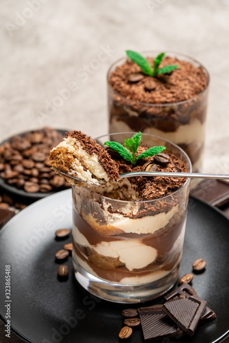 Classic tiramisu dessert in a glass cup and pieces of chocolate on concrete background