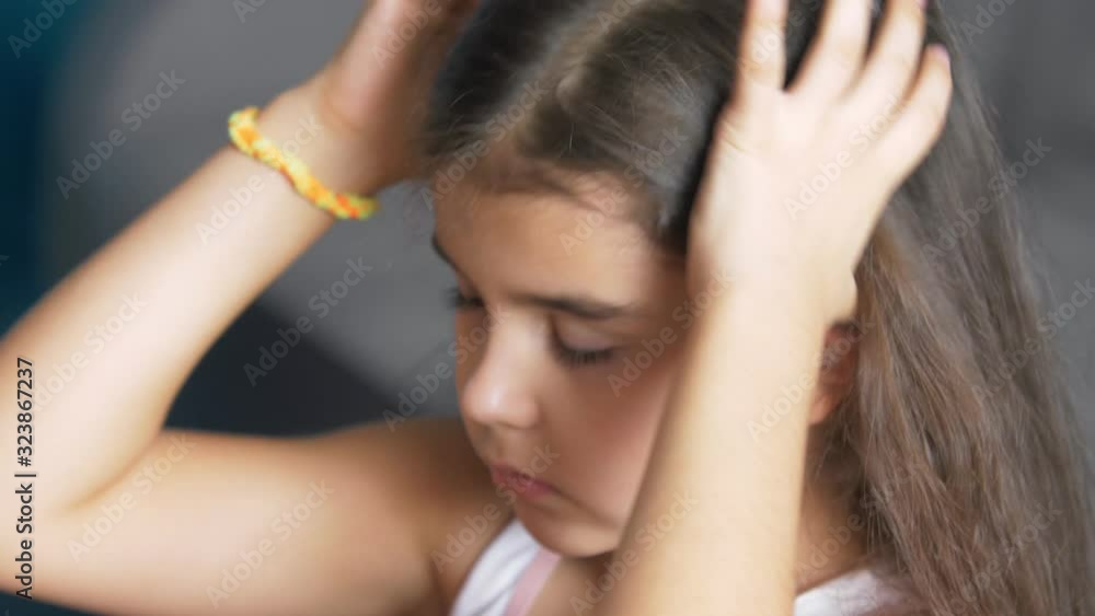 Little child girl collects her hair in a ponytail. Pulls the ponytail with a hair band. Wear a headband. Girl does her hair. Long beautiful curly hair. Close up Little child girl collects her hair in a ponytail. Pulls the ponytail with a hair band. Wear a headband. Girl does her hair. Long beautiful curly hair. Close up