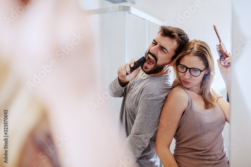 Attractive caucasian couple standing in bathroom in the morning, having fun and singing.