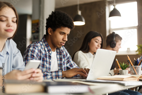 College groupmates studying in library, guy using laptop