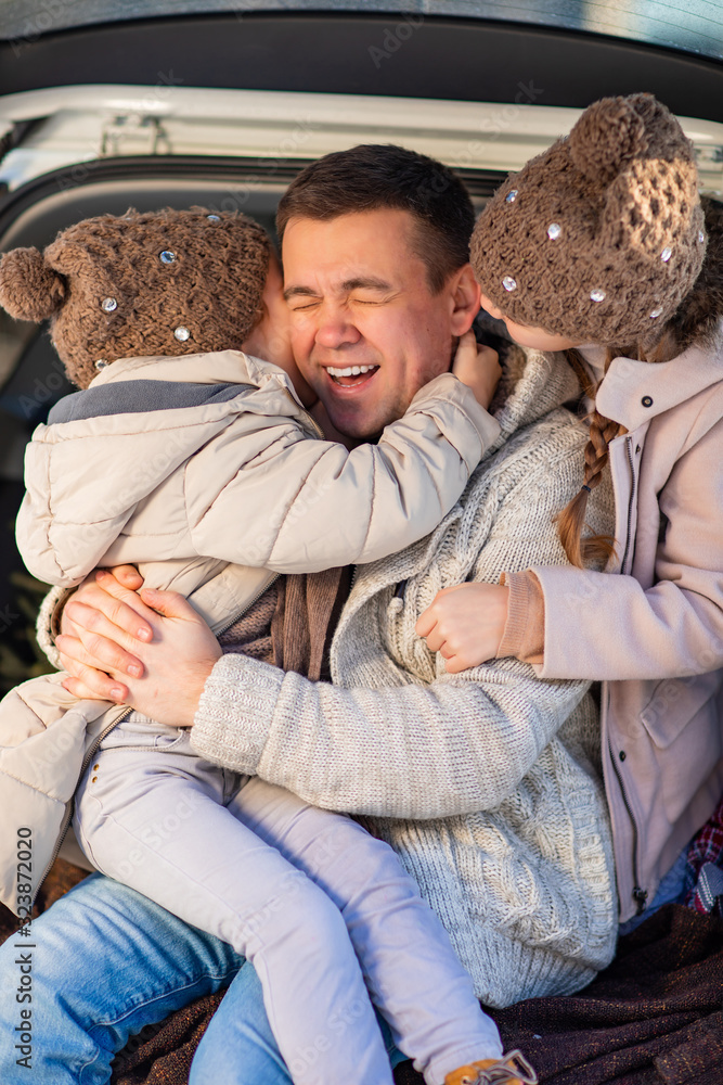 Fototapeta premium dad and daughters sitting in the trunk of a car 