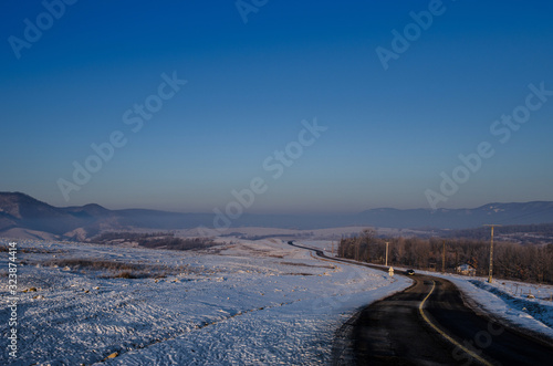 Frozen road passing through a hilly winter landscape, at sunrise