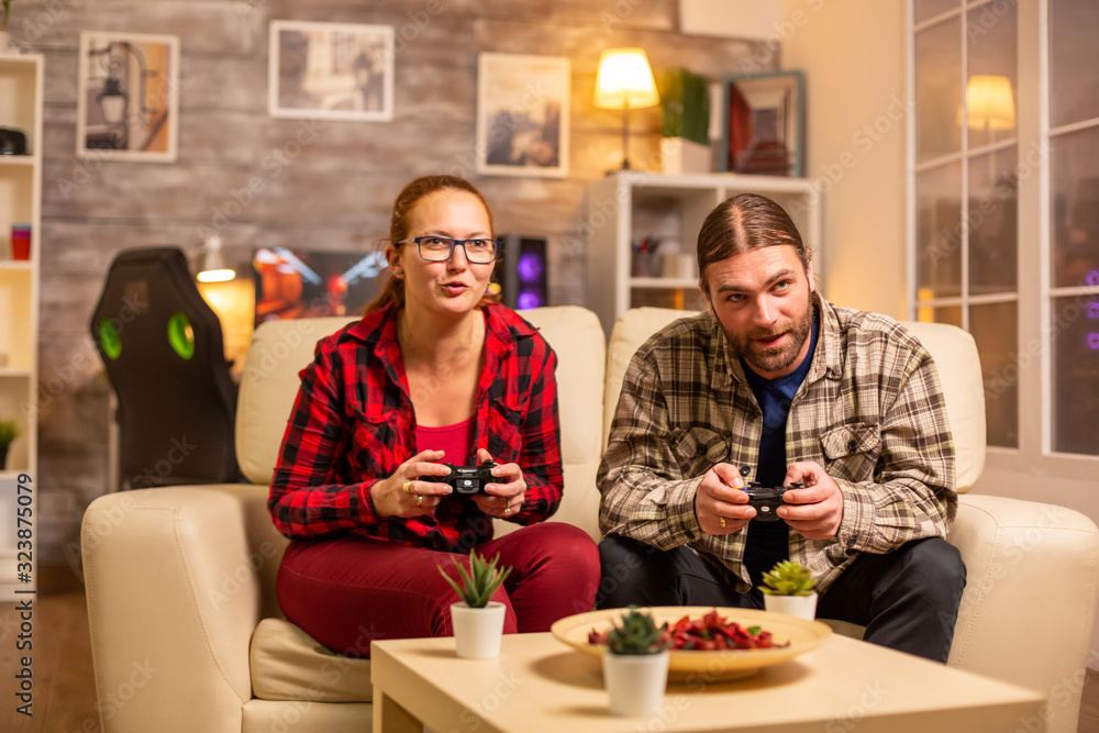 Gamers couple playing video games on the TV with wireless controllers in hands