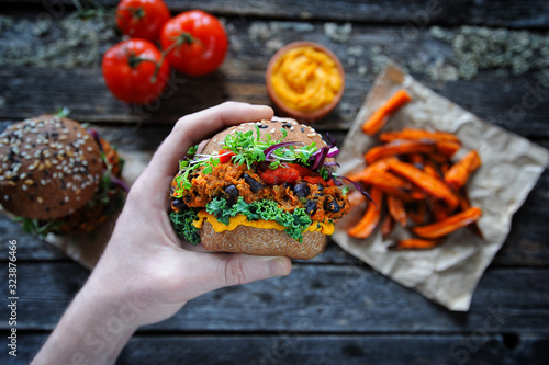 Hand holding vegan sweet potato black bean burger. Plant based food concept
