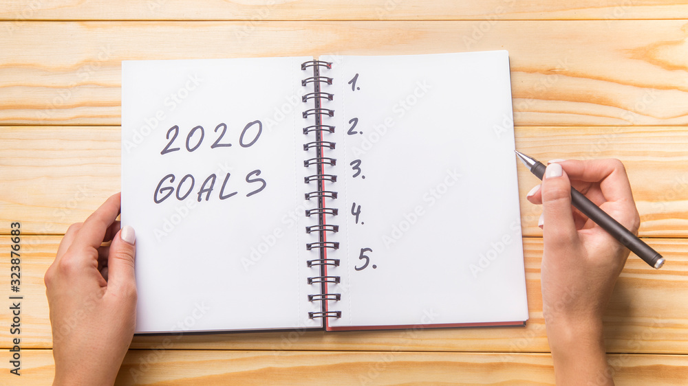 Woman writing in planner 2020 goals, wooden table Woman writing in planner 2020 goals, wooden table