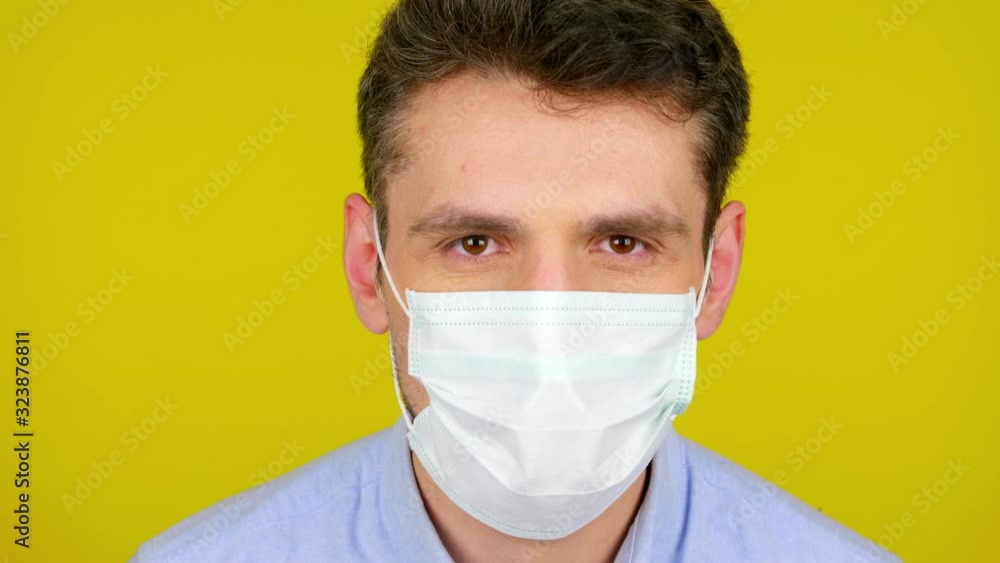 Young man puts on a medical mask on yellow background with copy space. Epidemic precautions. Acute Respiratory Virus Infection. Illness cold flu. Protective mask. 4K footage. Close-up. Young man puts on a medical mask on yellow background with copy space. Epidemic precautions. Acute Respiratory Virus Infection. Illness cold flu. Protective mask. 4K footage. Close-up.