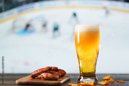 Spicy barbecue chicken wings, nachos and beer on dark wooden bar table. Football on background, high resolution