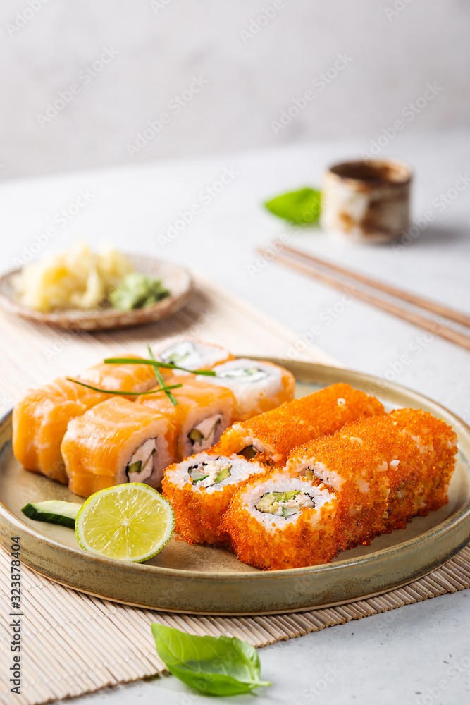 Set of sushi and maki on plate with soy sauce and chopsticks on white background. Top view with copy space