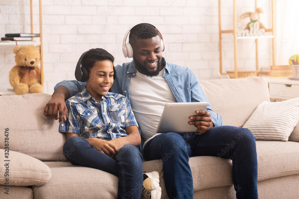 Cheerful Black Father And Son Watching Funny Videos On Digital Tablet - obrazy, fototapety, plakaty 