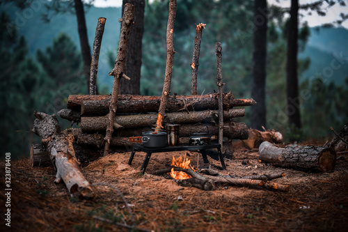 Primitive Bushcraft survival debris hut with campfire ring outside. Blanket, shelter, fire in the forest. photo