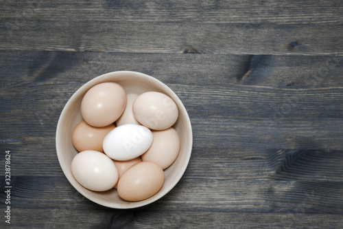 Chicken eggs in a light wooden bowl on a dark wooden table. Background. The concept of healthy farm egg production