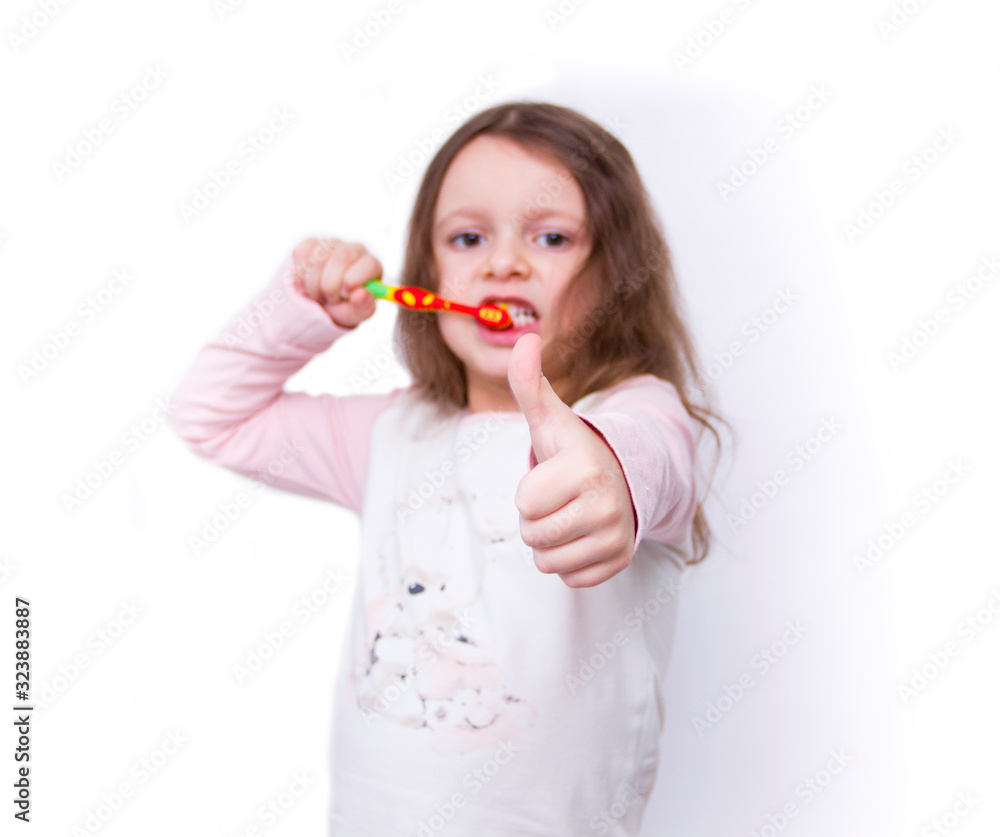 Cute little girl in pajamas brushing her teeth with a colored toothbrush isolated on white background. Cute little girl in pajamas brushing her teeth with a colored toothbrush isolated on white background.