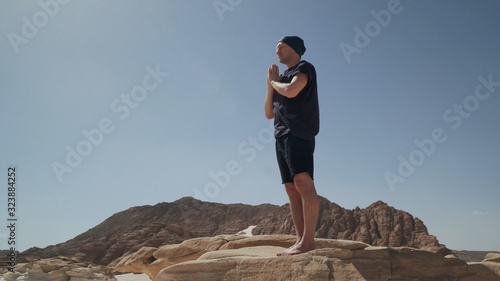 Handsome male staying in tadasana doing namaste on a rock in desert photo