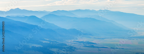Mountains in blue haze, panoramic view. Peaks in the clouds, valley and mountainsides.