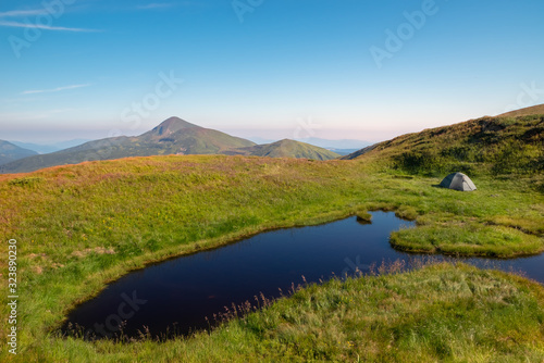 A mountain lake near which a tourist tent is set against the backdrop of the Hoverla mountain. Mountain landscape.