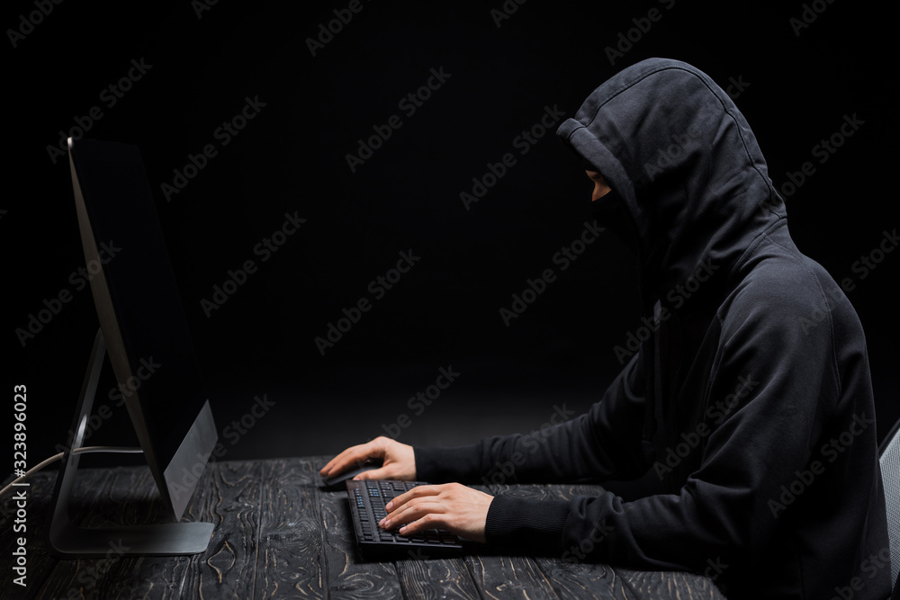 hacker in hood looking at computer monitor with blank screen on black hacker in hood looking at computer monitor with blank screen on black
