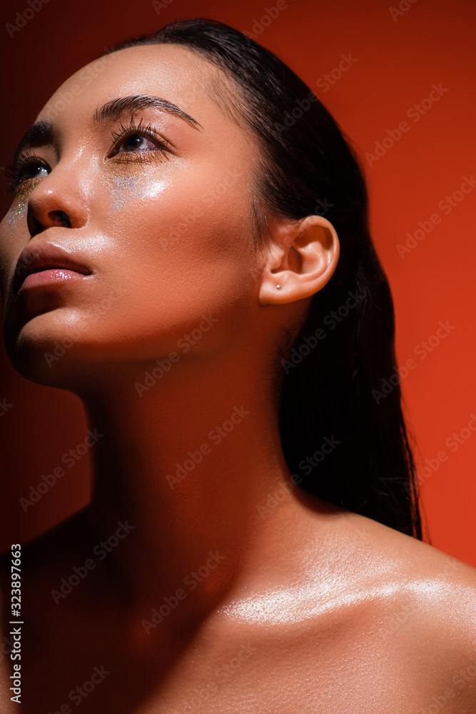 low angle view of beautiful naked asian girl with silver sparkles on face on red low angle view of beautiful naked asian girl with silver sparkles on face on red