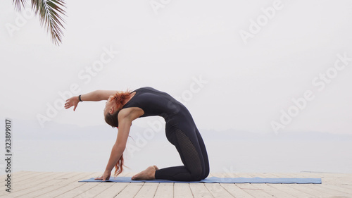 Handsome female doing hatha yoga asana at sea on foggy sunrise photo